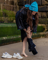 1|Woman crouched down getting changed, wearing Black Blue dryrobe® Advance Short Sleeve