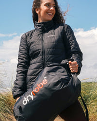 Woman holding dryrobe® Compression travel bag stood on the beach