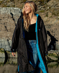1|Woman stood on beach, wearing unzipped Black Blue dryrobe® Advance Long Sleeve