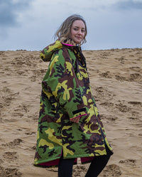 1|Girl smiling at camera walking on beach, wearing Camo Pink dryrobe® Advance Kids Long Sleeve