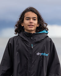 1|Close up of boy stood outdoors, wearing Black Blue dryrobe® Advance Kids Long Sleeve