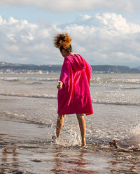 Girl running through the shoreline at the beach, wearing Kids Towel Poncho in Pink