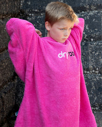 Boy stood in front of a wall, wearing Kids Towel Poncho in Pink