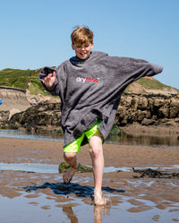 Boy running through water on the beach, wearing Kids Towel Poncho in Slate Grey