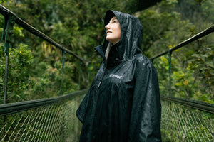 B Corp Month logo layered on a photo of a woman in the rainforest wearing a dryrobe Lite