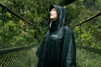 B Corp Month logo layered on a photo of a woman in the rainforest wearing a dryrobe Lite