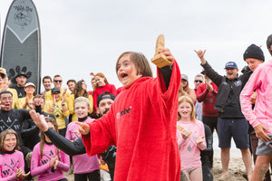 AWOW Athlete wearing a red dryrobe® Towel and holding a trophy with people cheering around him