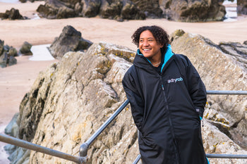 Mini Cho stood on Putsborough Beach wearing a dryrobe® and smiling 