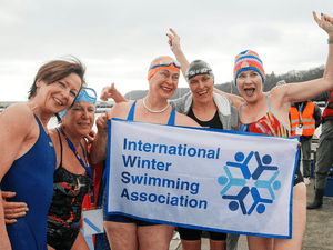 A group of female swimmer holding up an International Winter Swimming Association sign by an outdoor pool