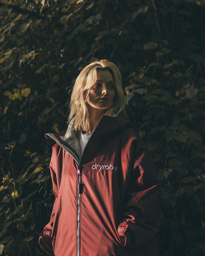 Female standing by hedge wearing AW25 Burgundy Dryrobe® advance long sleeve 