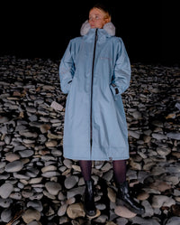 Woman stood on pebble beach at night, wearing dryrobe Advance Long Sleeve Alpine Range change robe in Alpine Ice Blue