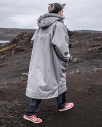 Man walking along cliff away from camera, wearing dryrobe Advance Long Sleeve Alpine Range change robe in Alpine Graphite 