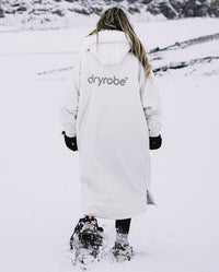 Woman walking through snowy mountain away from camera, wearing dryrobe Advance Long Sleeve Alpine Range change robe in Alpine White
