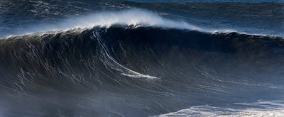 Andrew cotton surfing large wave crashing in the ocean with a dark blue color.