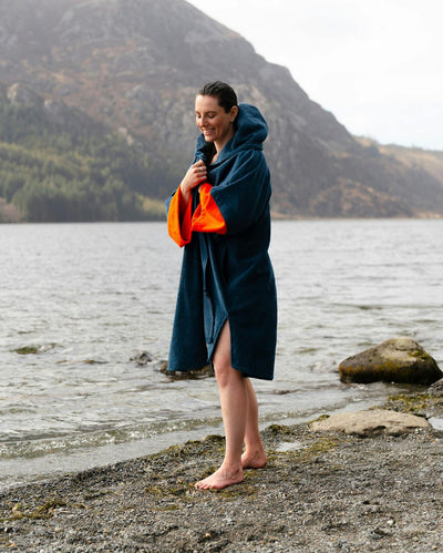 Female by water wearing Dryrobe® Zip towel (blue orange)