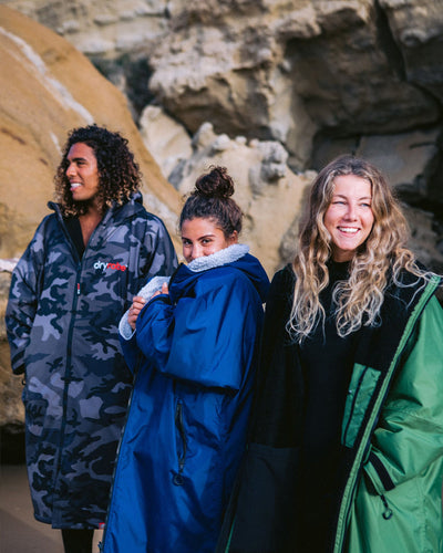 Three people wearing dryrobes standing on a rocky beach.