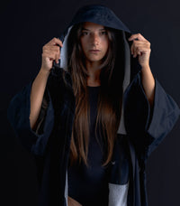 Woman wearing a dark hooded cloak against a black background