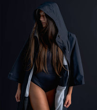 Person wearing a dark hooded coat over a black swimsuit against a dark background