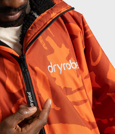 *MALE* Close-up of a person wearing an orange Dryrobe jwith a tonal orange camouflage pattern, black zipper, and white logo on the chest.