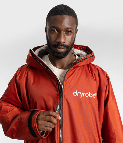 *MALE* A man wearing a red hooded dryrobe jacket with a white logo on the chest, photographed against a light gray studio background.
