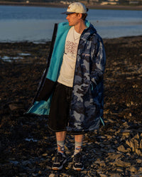 **MALE** Man stood on a beach wearing a cap and dryrobe Advance Long Sleeve changing poncho in Blue Camo Blue