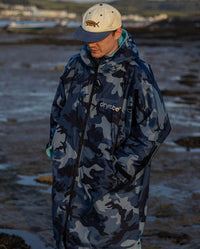 **MALE** Man stood on a beach wearing a dryrobe Advance Long Sleeve changing poncho in Blue Camo Blue