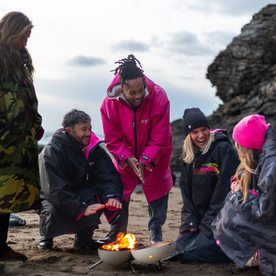Group of people wearing Dryrobe® changing robes around a fire pit on a beach