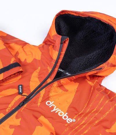 Close-up of a hooded Dryrobe in bright orange and orange-red camouflage with a black fleece-lined hood and black zipper, on a white background.