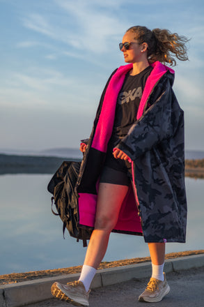 Person wearing a black and pink dryrobe by a body of water
