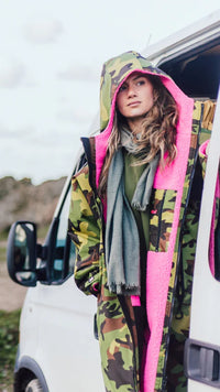 Person wearing a colorful camo pink Dryrobe® changing robe with pink accents standing next to a white van.