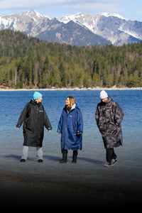 Three people wearing Dryrobes standing by a lake with mountains in the background
