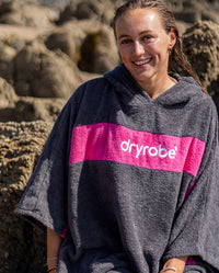 Woman smiling in the sun on a beach wearing Organic Towel dryrobe Remix in Slate Grey Pink