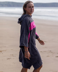 Woman walking towards the sea on a beach wearing Organic Towel dryrobe Remix in Slate Grey Pink