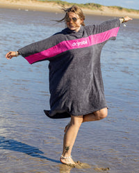 Woman jumping with arms out to the side on a beach wearing Organic Towel dryrobe Remix in Slate Grey Pink