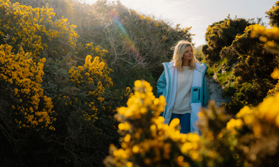 Woman standing among yellow flowers and greenery wearing a blue dryrobe