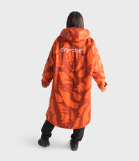 A person shown from the back wearing a long hooded orange Dryrobe with an allover abstract pattern and the brand name 'dryrobe' printed in white across the upper back, against a light gray studio background.