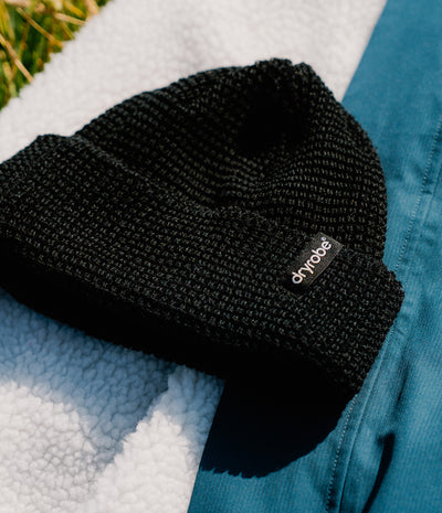 A black ribbed knit beanie with a small black brand tab reading 'chyroes' in white text, styled on a white sherpa fabric next to a teal garment.