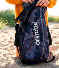 Person holding a camouflage backpack with 'dryrobe' branding on a sandy background