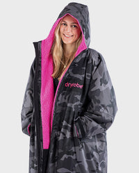 Close up of woman smiling wearing dryrobe Advance Long Sleeve REMIX Range change poncho in Black Camo Pink Black with hood up 