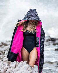 Woman walking along beach, wearing dryrobe Advance Long Sleeve REMIX Range change poncho in Black Camo Pink Black