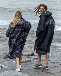 Two people walking to the sea wearing dryrobe Advance Long Sleeve REMIX Range