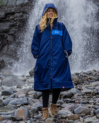 Woman stood in front of waterfall, wearing dryrobe Advance Long Sleeve REMIX Range change poncho in Navy Grey Cobalt 