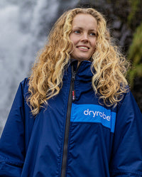 Close up of woman stood in front of waterfall, wearing dryrobe Advance Long Sleeve REMIX Range change poncho in Navy Grey Cobalt 