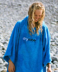 Woman with wet hair smiling on a beach, wearing Cobalt Blue Organic Towel dryrobe®