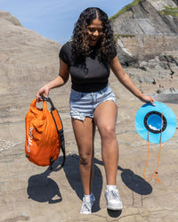 Woman smiling on beach, holding dryrobe Quick Dry Brimmed Hat and dryrobe Compression Travel Bag