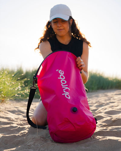 Woman on beach unpacking hot pink Dryrobe® compression bag 