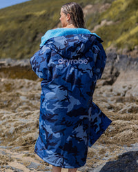 Woman on a beach with back to the camera, wearing dryrobe Advance Long Sleeve changing poncho in Blue Camo Blue