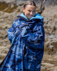 Woman on a beach wearing dryrobe Advance Long Sleeve changing poncho in Blue Camo Blue, wrapping it around herself 