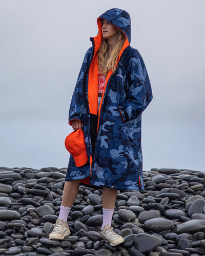 Woman stood on rocks, wearing Blue Camo Orange dryrobe advance long sleeve changing robe with hood up  