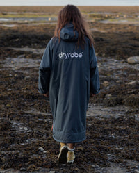 Woman walking along seaweed on beach,  wearing dryrobe Advance Long Sleeve change poncho in Dark Grey Orange